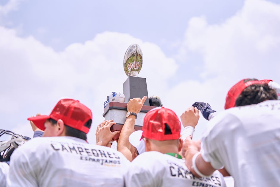 Group of athletes lifting a championship trophy outdoors in celebration.